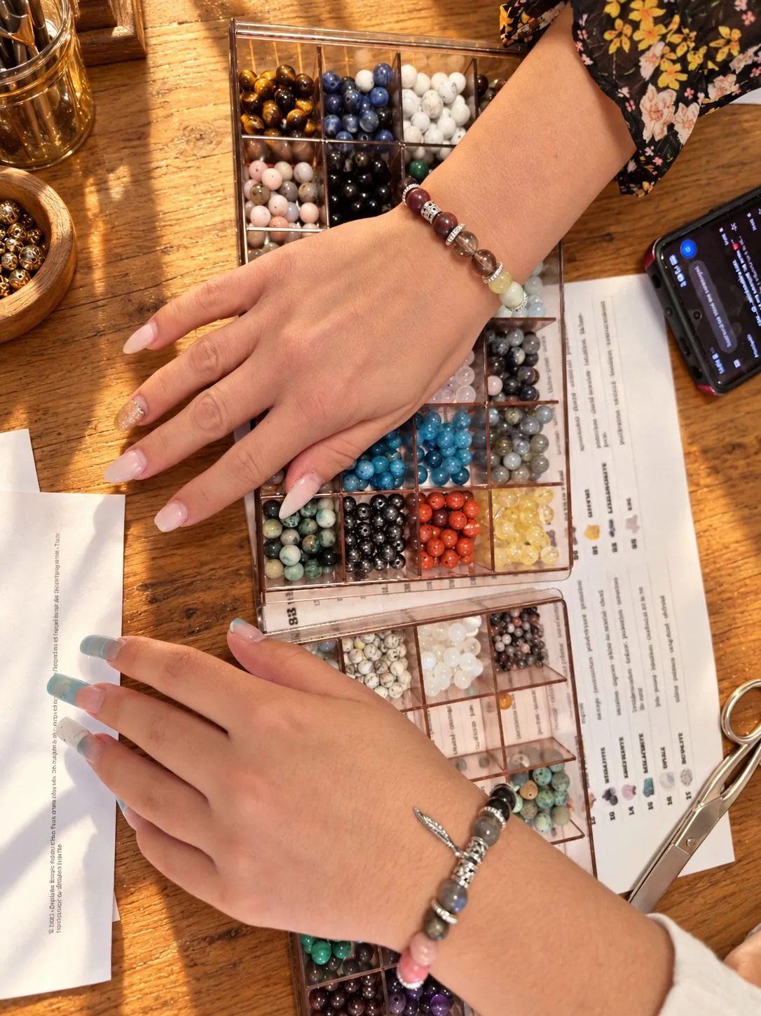 Deux poignets avec leurs bracelets en pierres naturelles au-dessus des boîtes de perles, atelier bijoux 77